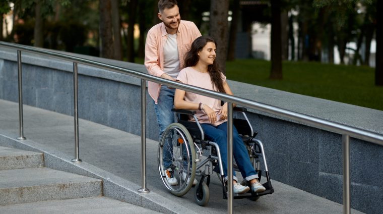 Love couple with wheelchair walking in autumn park. Paralyzed people and disability, care for a disabled woman. Smiling husband and wife overcome difficulties together