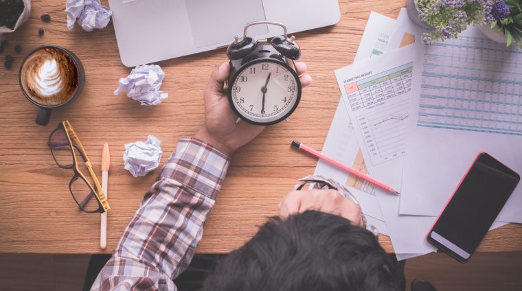 wood-table-with-businessman-holding-alarm-clock-late-payment-view-from-office-table